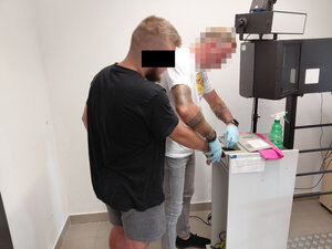 Policjant pobiera odbitki palców na urządzeniu elektronicznym od zatrzymanego mężczyzny