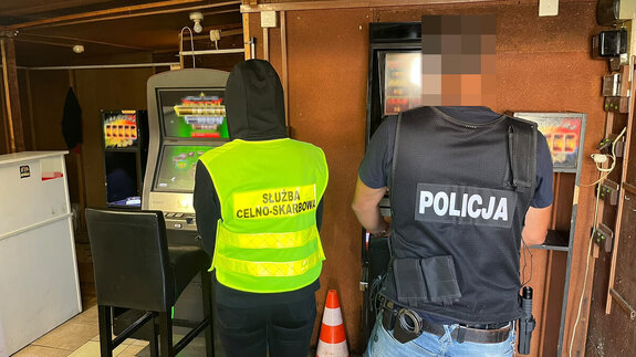 Policjant i funkcjonariusza służby celno-skarbowej stoją przy automatach do gier