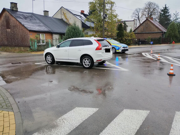Zdjęcie z miejsca zdarzenia drogowego na drodze stoi biale volvo a pod jego spodem leży rower uszkodzony